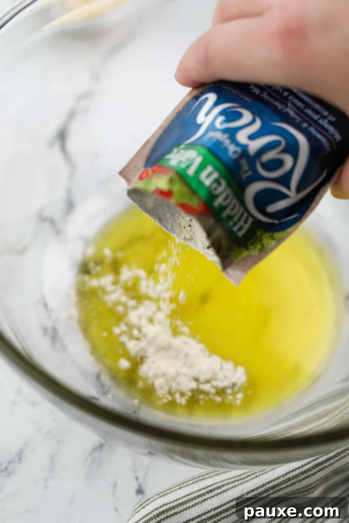 Zesty Ranch Roasted Broccoli 5 A hand sprinkling dry ranch seasoning directly into a bowl of olive oil.