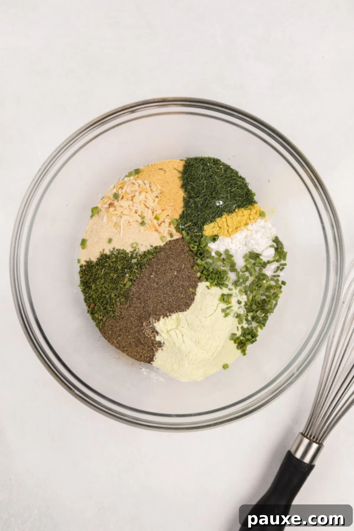 A medium mixing bowl filled with an assortment of dried herbs, garlic powder, onion powder, and salt, ready for mixing.