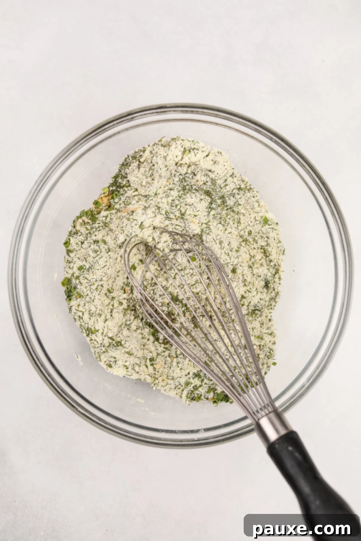 A close-up shot of a hand whisking together the dry ingredients for ranch seasoning in a bowl, showcasing the blending process.