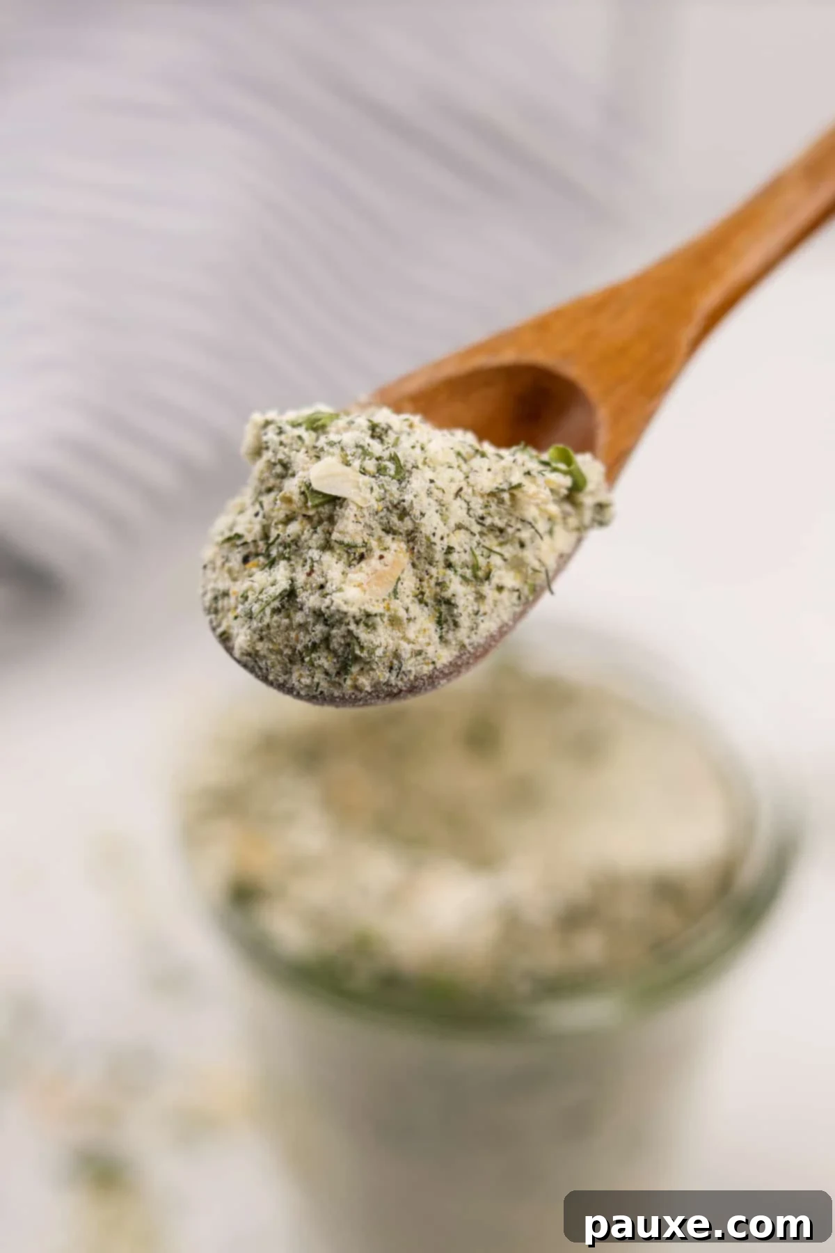 A small wooden spoon carefully scooping out homemade ranch seasoning from a glass jar, showing the mix up close.