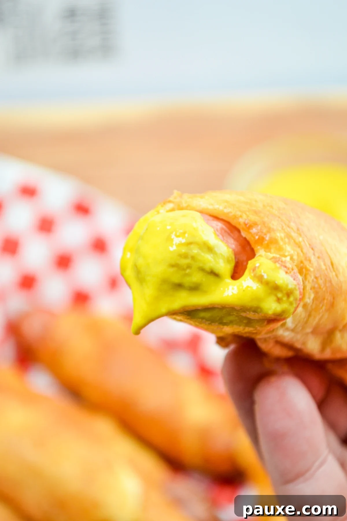 Air Fryer Pigs in a Crispy Blanket 3 A pig in a blanket, dipped in bright yellow mustard, showcasing its golden brown exterior.