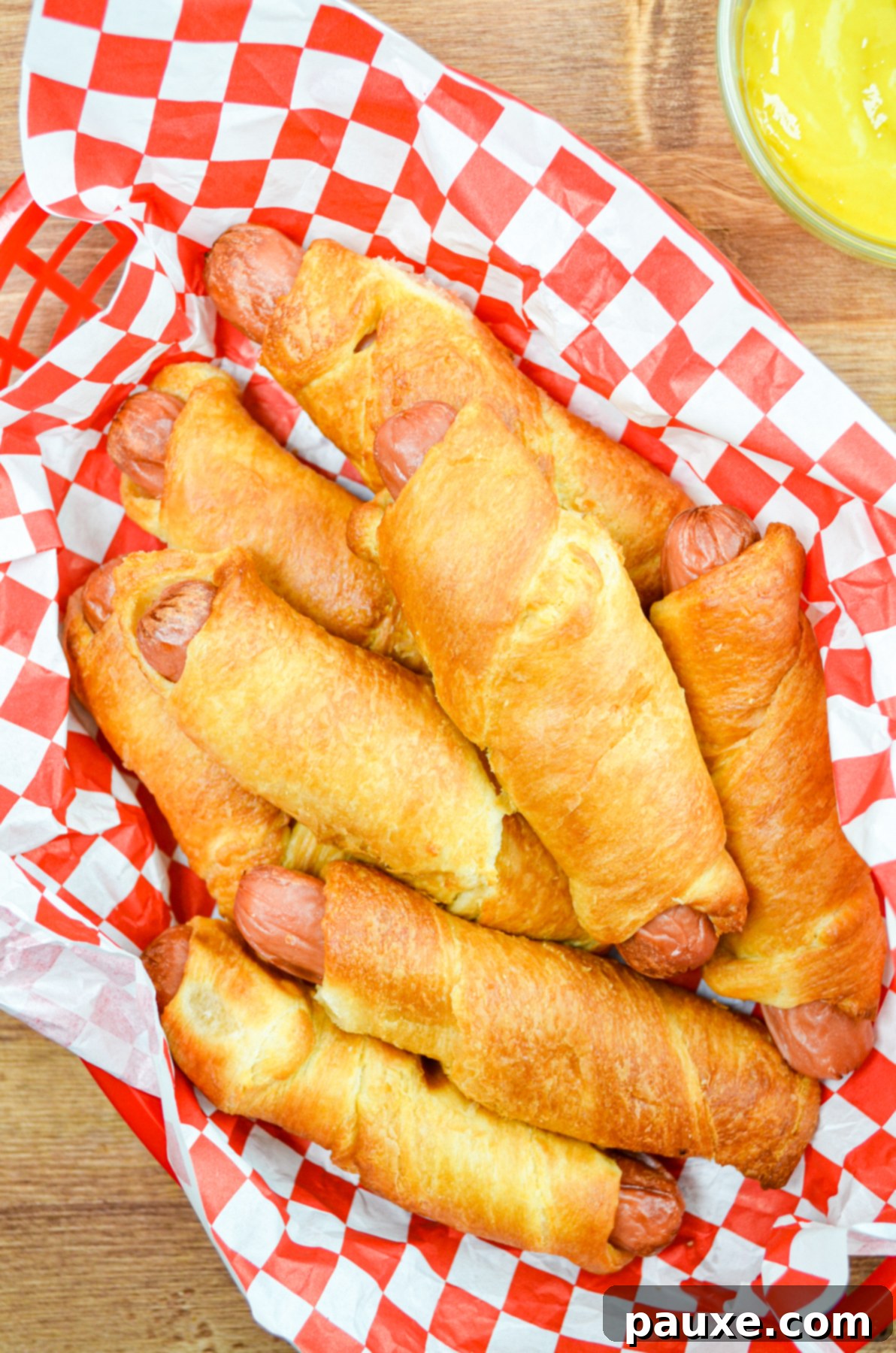 Air Fryer Pigs in a Crispy Blanket 9 A basket full of air fryer pigs in a blanket, with a small dish of bright yellow mustard on the side.