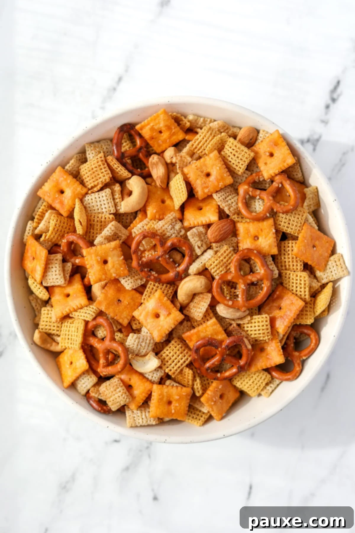 Effortless Slow Cooker Party Mix 11 A bowl of freshly made Chex Mix on a white background, showcasing its golden color and various components.