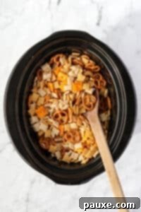 Effortless Slow Cooker Party Mix 14 A wooden spoon stirring dry Chex Mix ingredients in a crock pot.