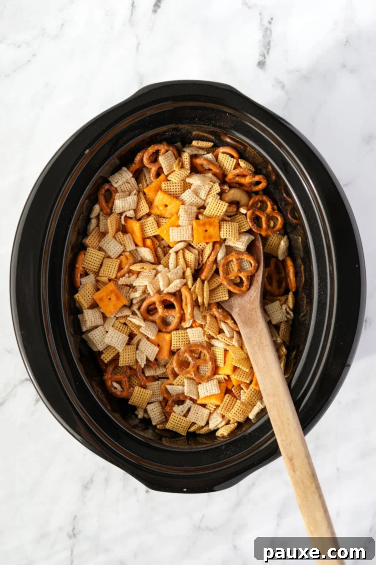 Effortless Slow Cooker Party Mix 5 A wooden spoon gently stirring a crock pot full of dry Chex Mix ingredients.