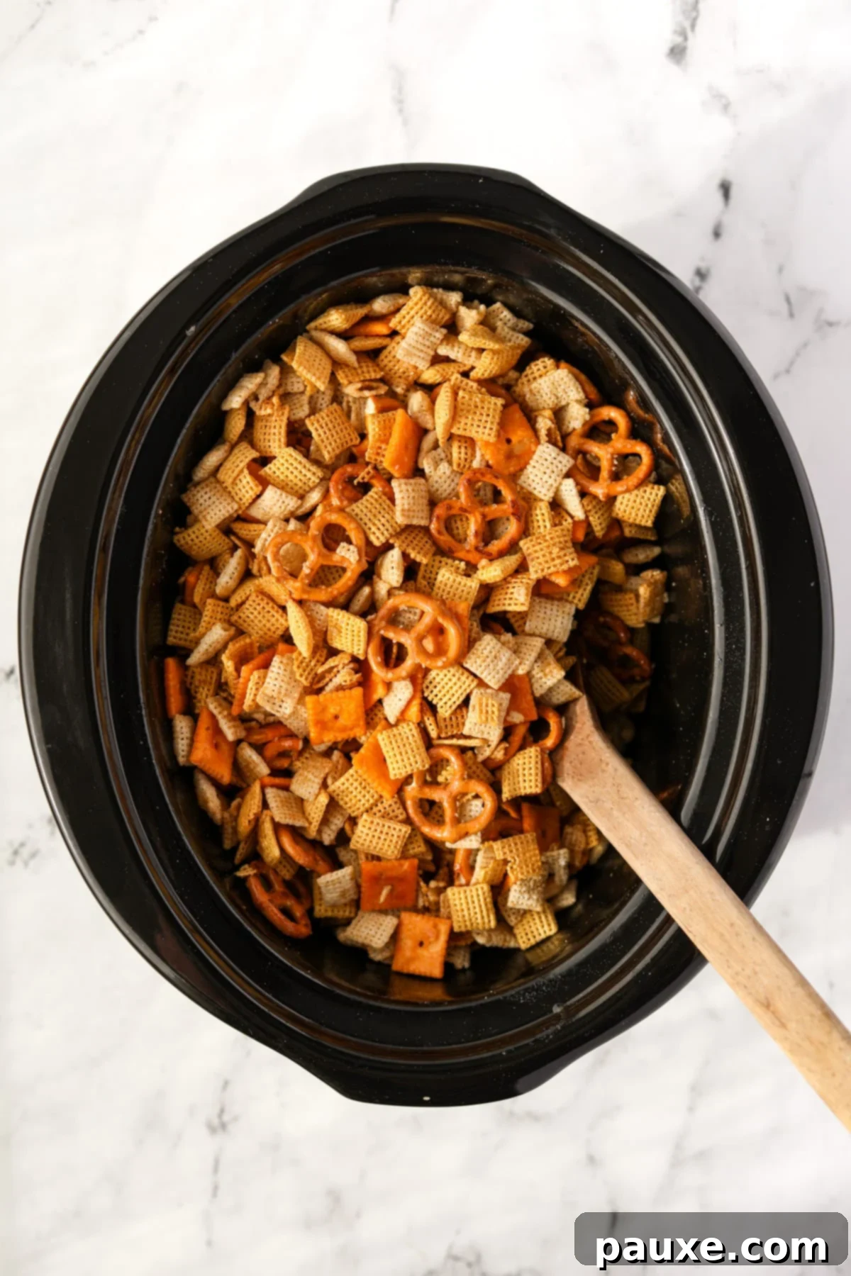 Effortless Slow Cooker Party Mix 8 A wooden spoon stirring Chex Mix in a slow cooker, showing the even coating of seasonings.