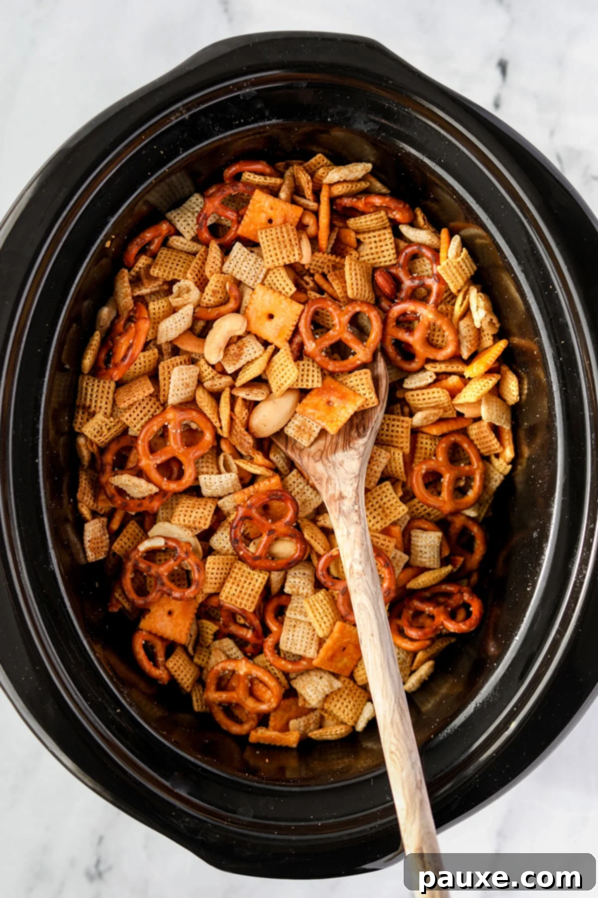 Effortless Slow Cooker Party Mix 9 Another angle of stirring Chex Mix in a slow cooker, emphasizing the thorough mixing process.