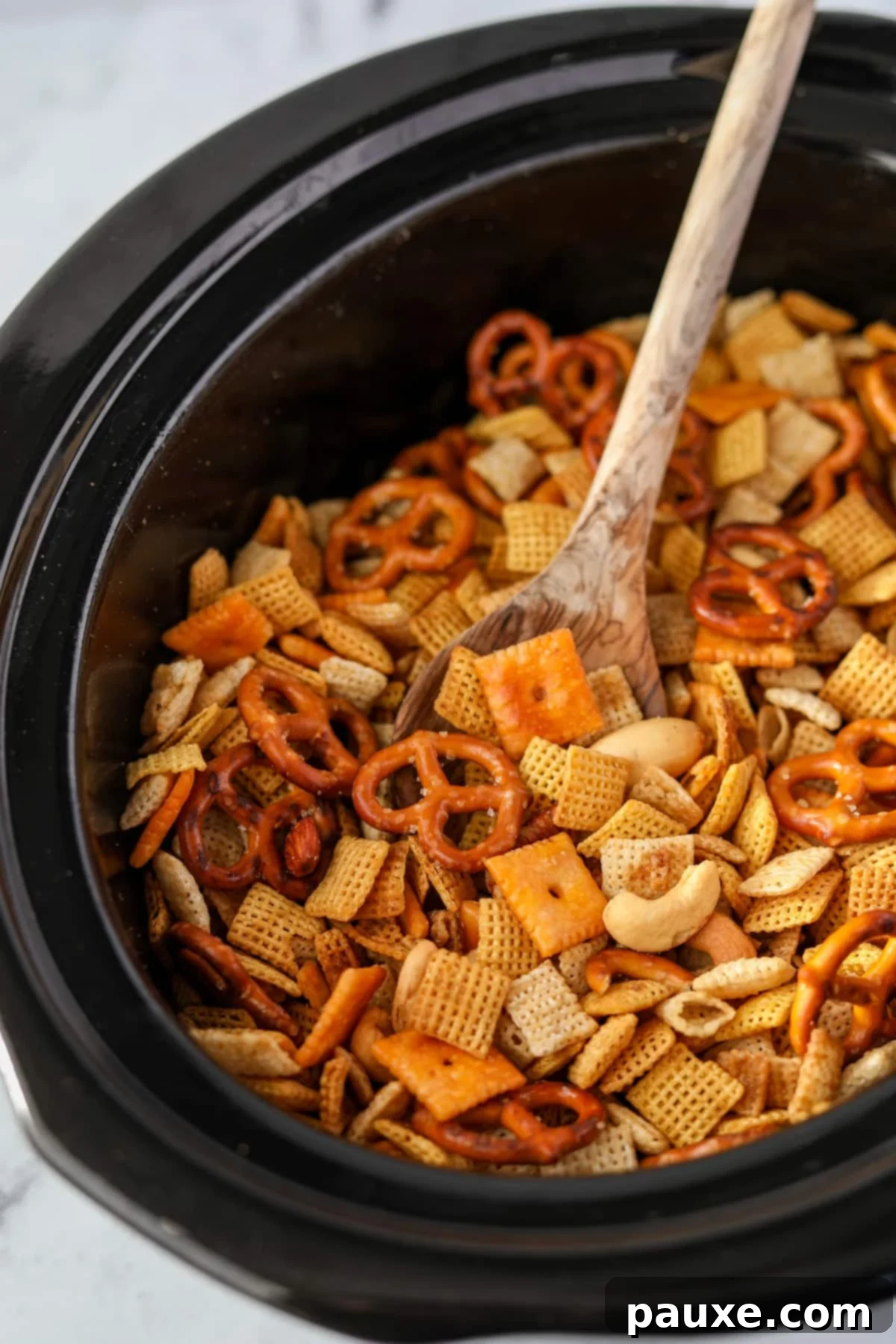 Effortless Slow Cooker Party Mix 10 A close-up of fully cooked and crispy Chex Mix being stirred in a slow cooker, ready to cool.