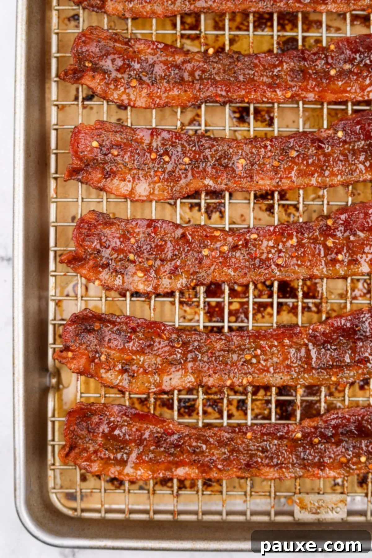 Decadent Glazed Bacon 2 Crispy Billionaire Bacon slices cooling on a wire rack, glistening with a sweet and spicy glaze.