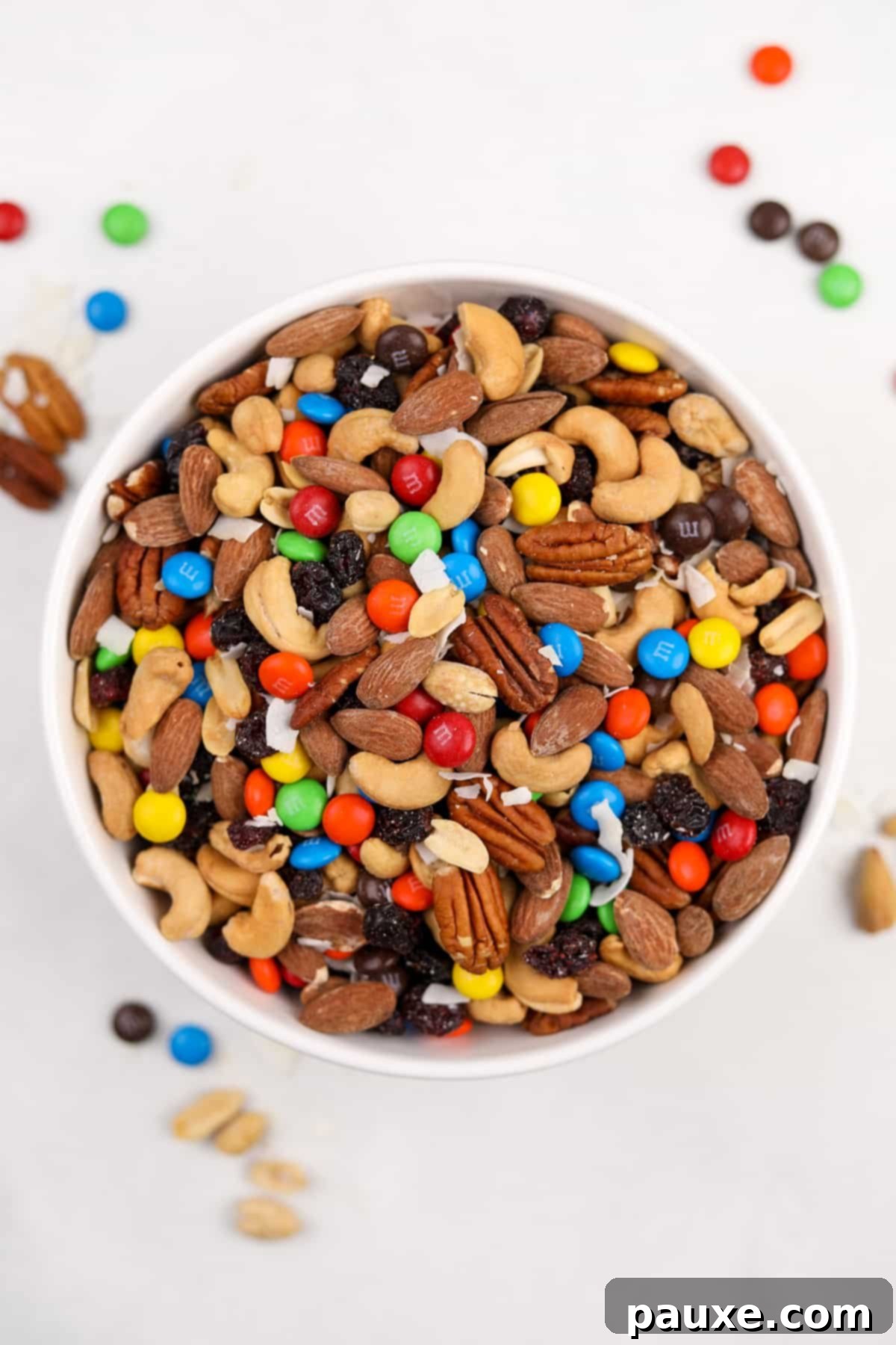 Trailblazer's Blend 2 A large bowl of homemade trail mix on a white surface, showcasing a variety of nuts, dried fruits, and candies.