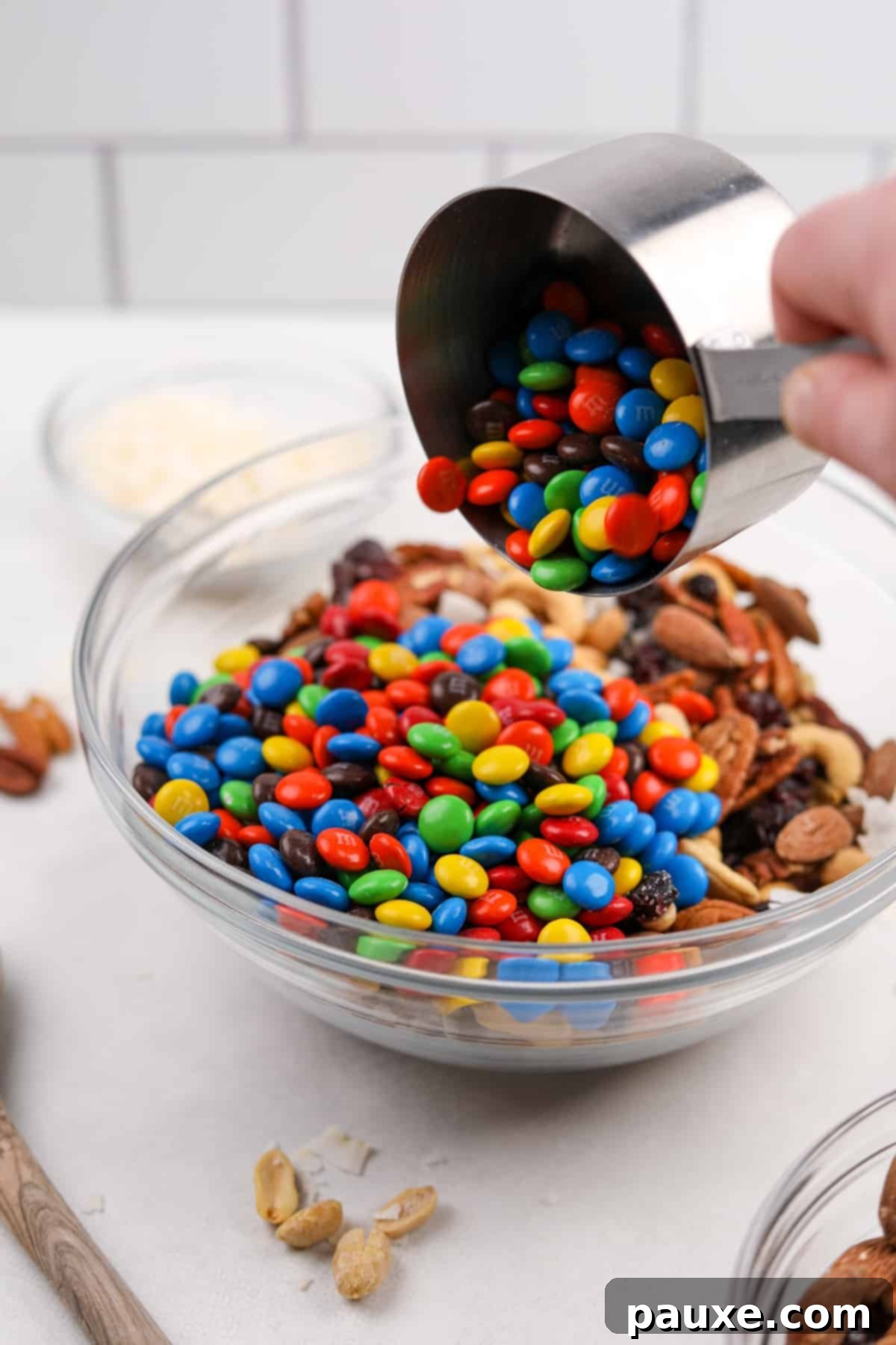 Trailblazer's Blend 6 Pouring M&M's into a bowl of mixed nuts and dried fruit.