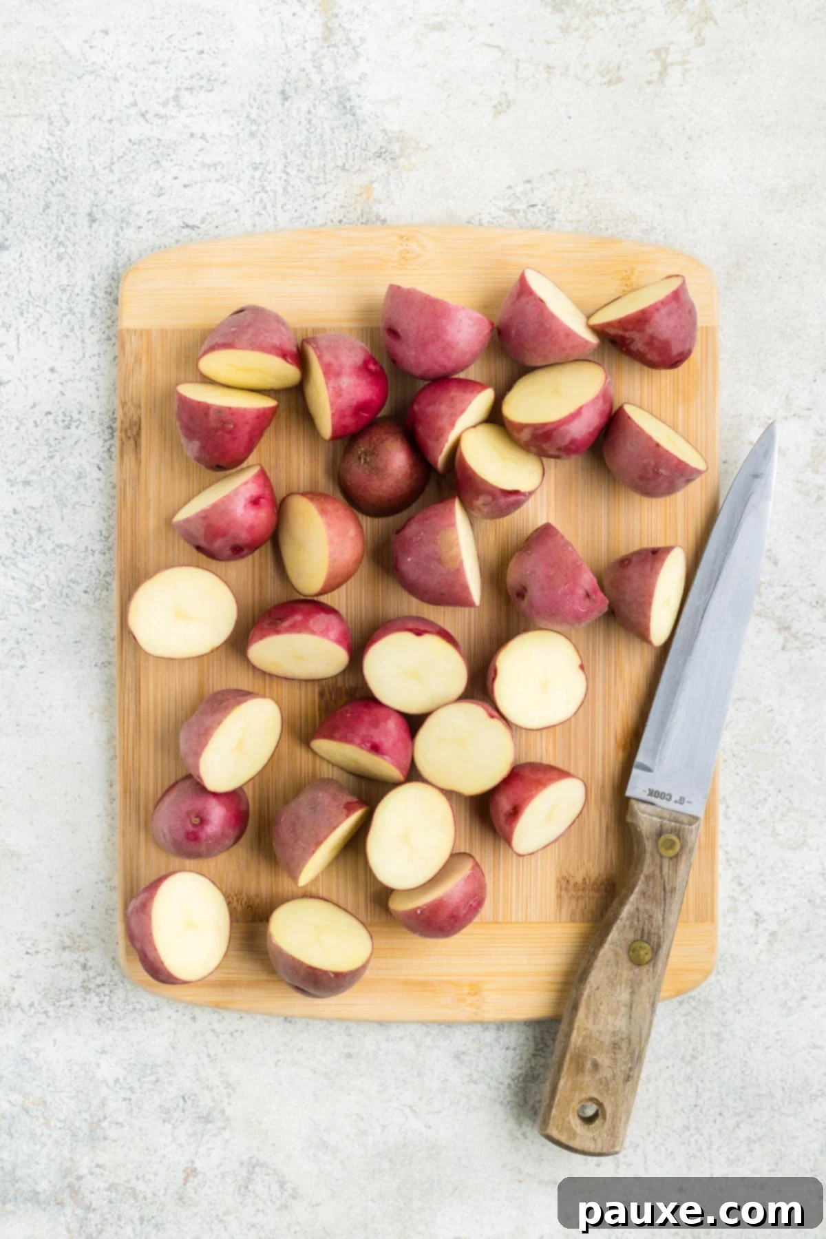 Slicing baby potatoes into uniform halves and quarters on a cutting board.