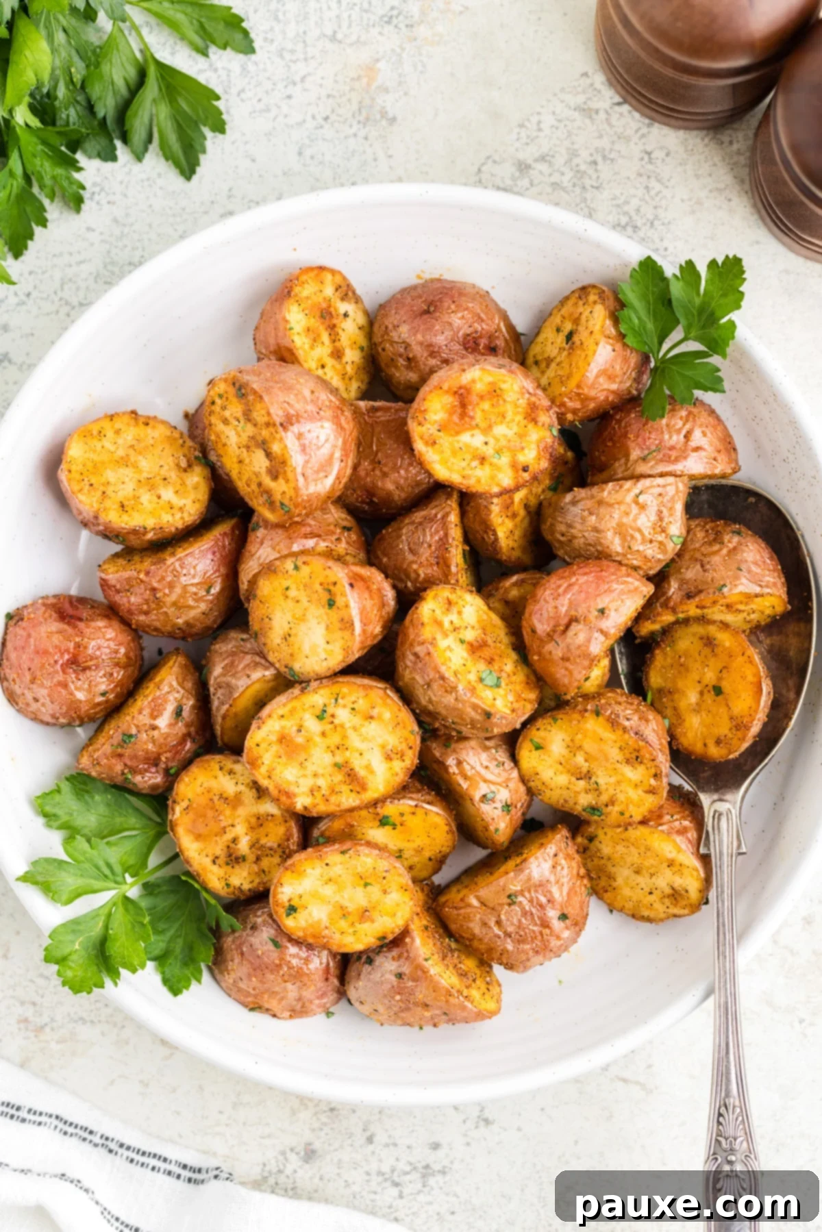 A white plate generously filled with golden, crispy roasted red potatoes, garnished with fresh green parsley.