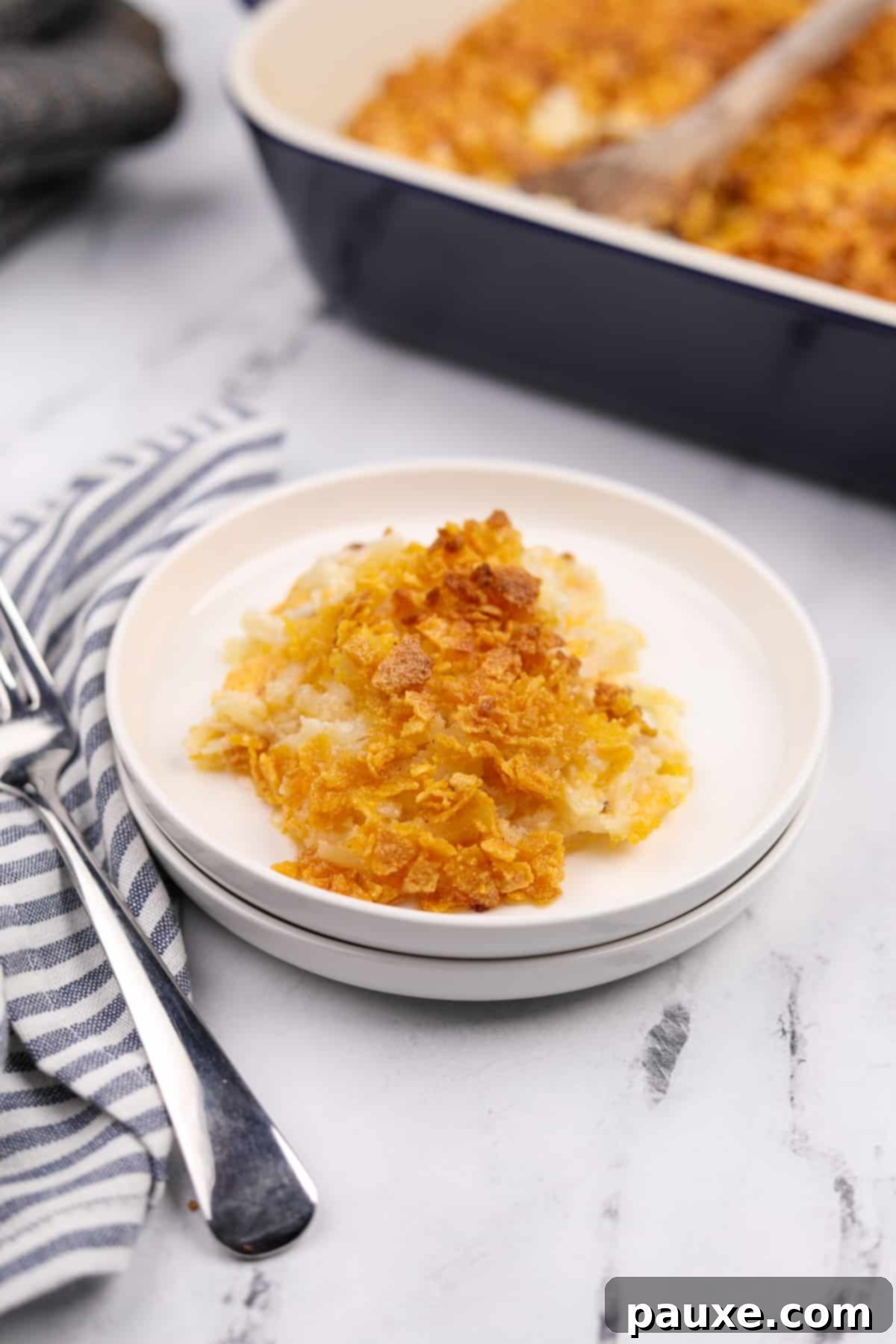 Gluten-Free Cheesy Hash Brown Casserole 16 A white plate with a perfectly portioned scoop of golden, cheesy gluten-free funeral potatoes, highlighting the rich texture and crispy topping.