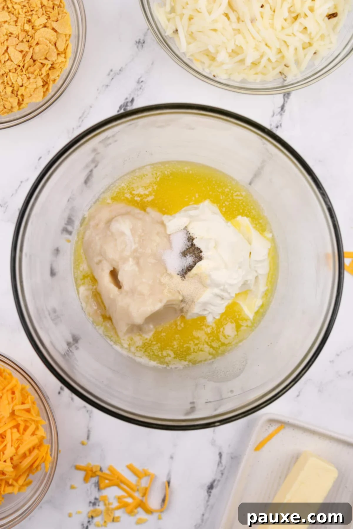 Gluten-Free Cheesy Hash Brown Casserole 4 A large mixing bowl containing melted butter, creamy sour cream, gluten-free condensed soup, and a sprinkle of seasonings, ready to be combined for the funeral potato base.