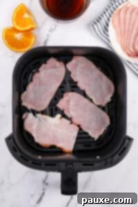 Easy Air Fryer Canadian Bacon 9 An air fryer basket with Canadian bacon slices placed inside, ready for cooking.