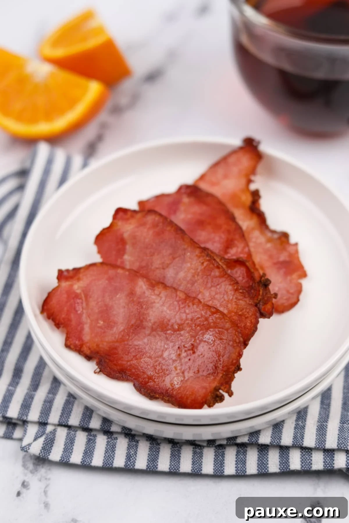 Easy Air Fryer Canadian Bacon 6 A charming plate resting on a striped napkin, holding four slices of golden-brown Canadian bacon.