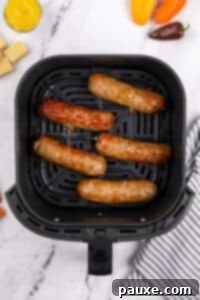 An air fryer basket with cooked sausages inside.