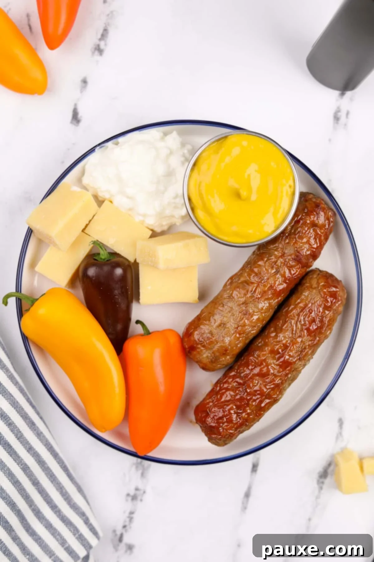 A beautifully presented plate showcasing air-fried chicken sausages, surrounded by an array of colorful vegetables, a side of mustard, and a serving of cottage cheese, highlighting a balanced meal.
