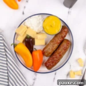 A beautifully arranged plate featuring crispy air-fried chicken sausages, accompanied by vibrant vegetables, a side of creamy cottage cheese, and a dollop of zesty mustard.