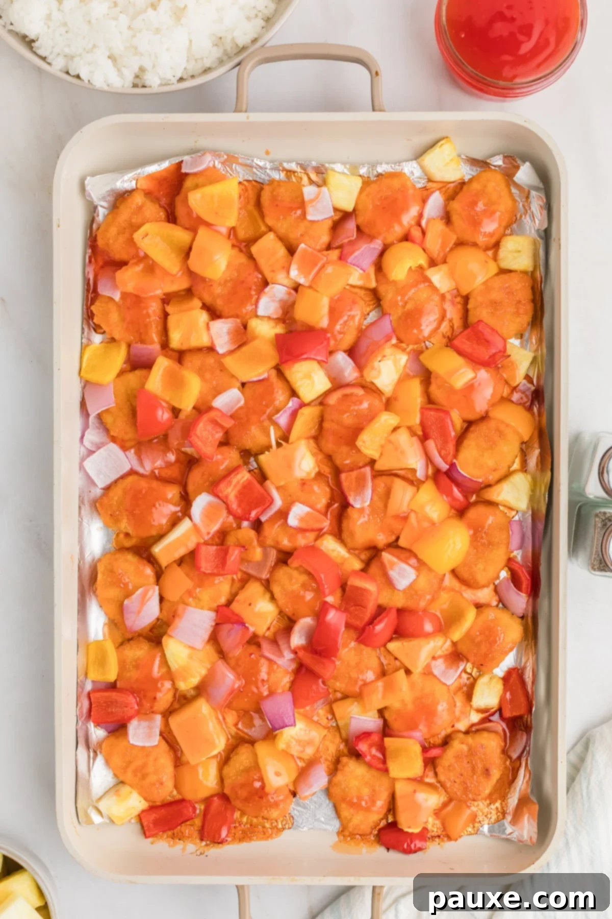 Sheet pan with cooked sweet and sour chicken, pineapple, and bell peppers.