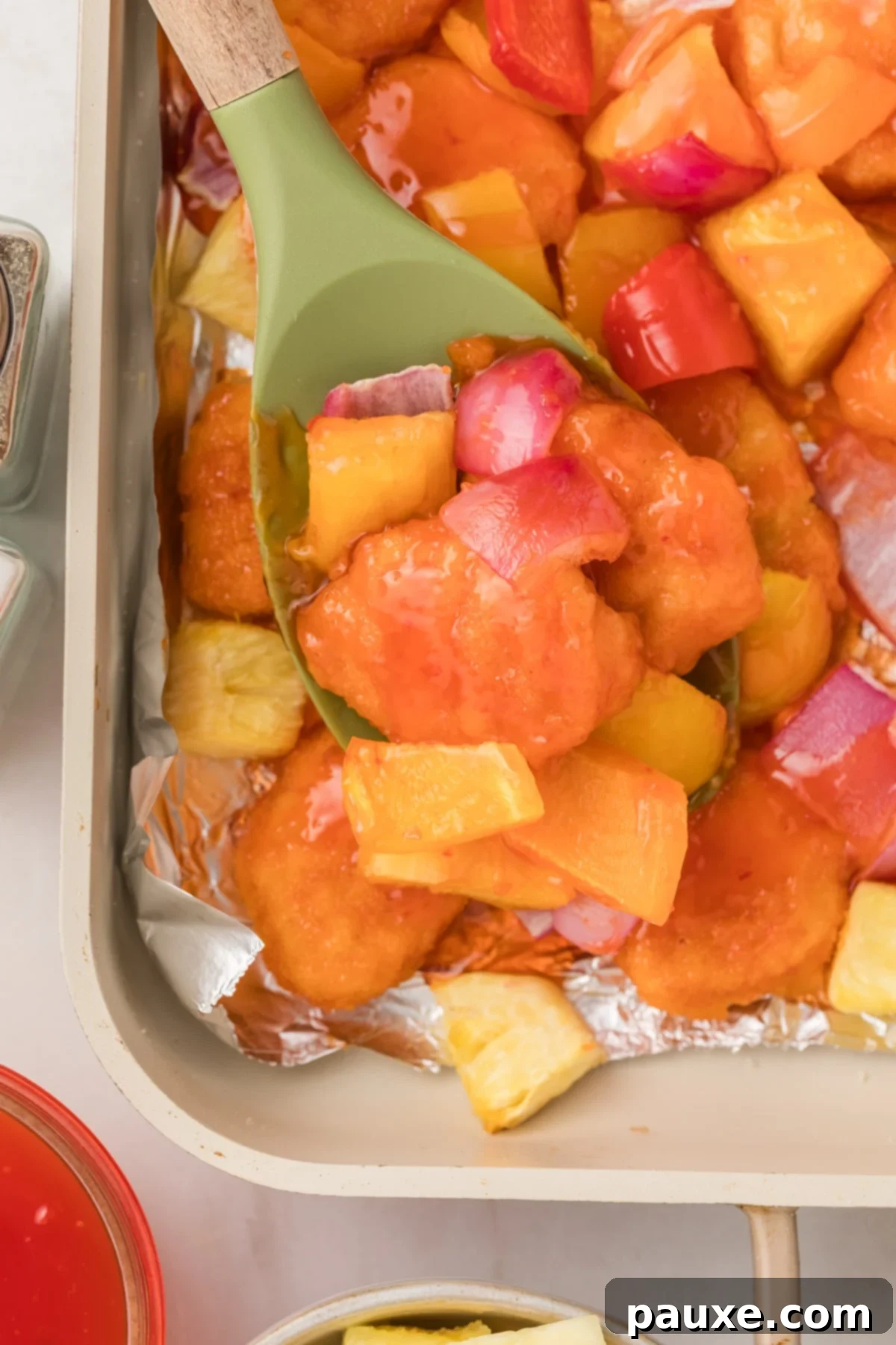 Spoon serving sweet and sour chicken from a sheet pan.