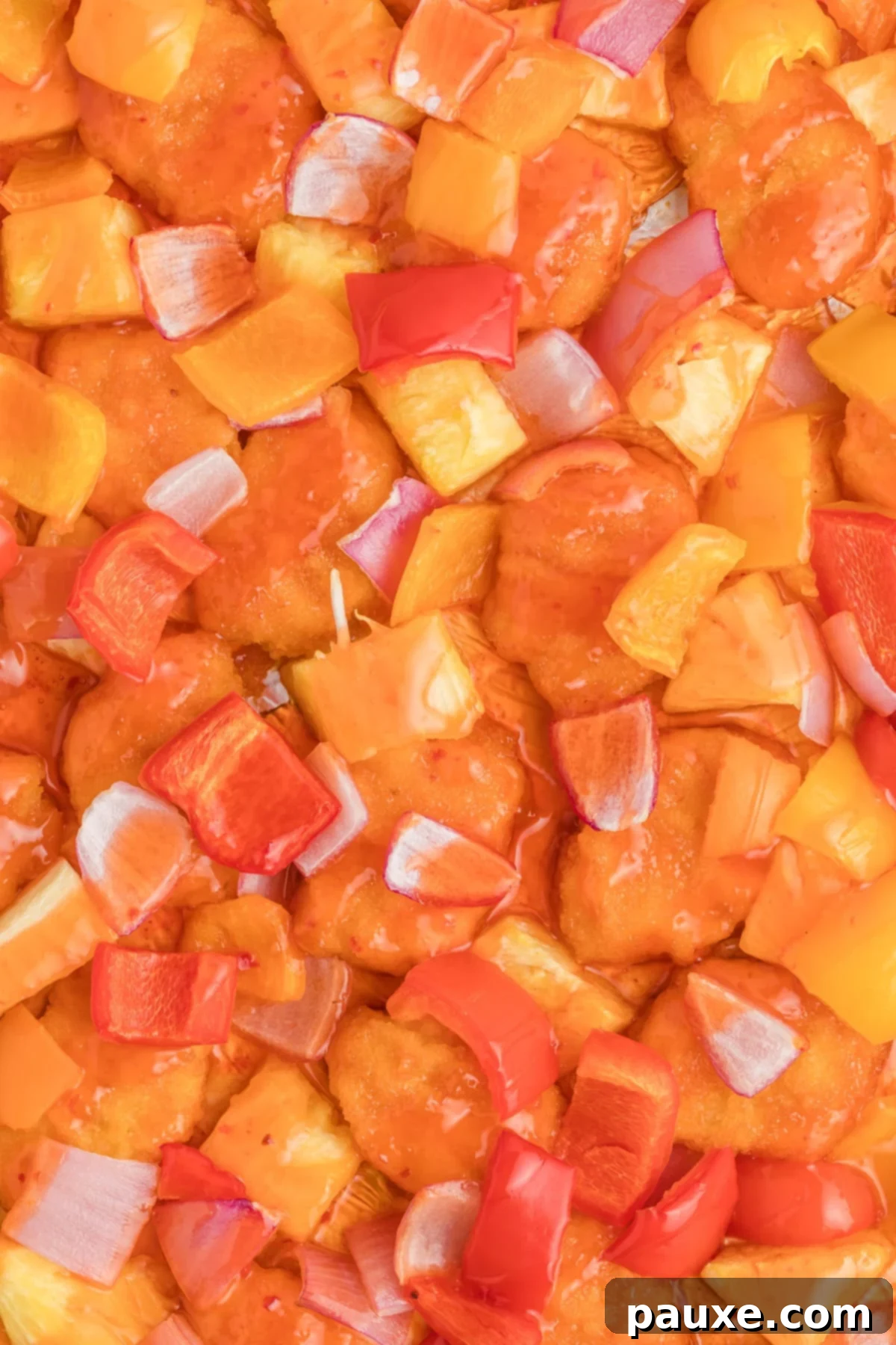 Chicken, pineapple, red onion, and bell peppers cooked in a shiny sauce on a sheet pan.